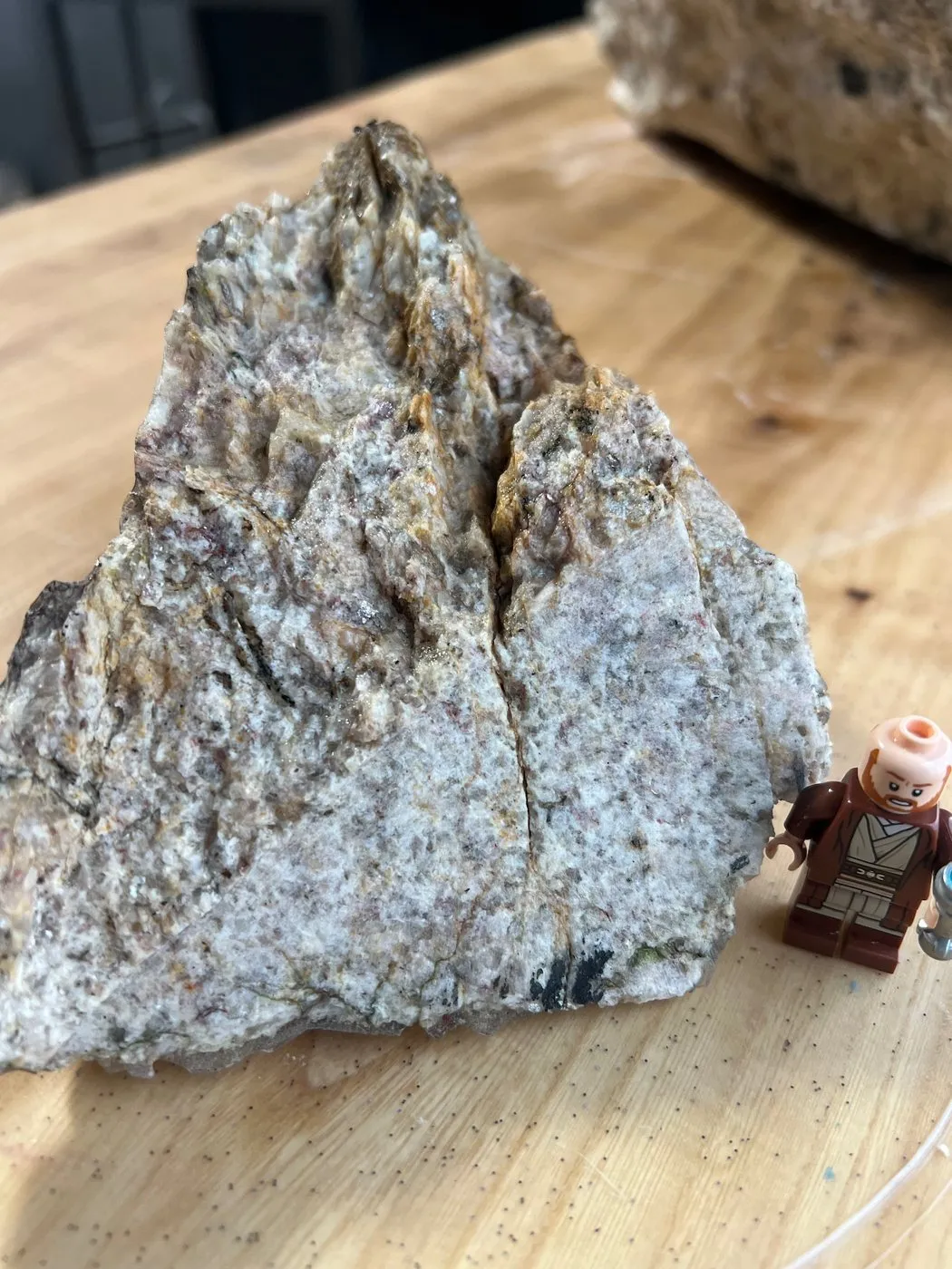 Raw piece of quartzofeldspathic mica schist with rust-stained mica seams, with a toy figure for scale