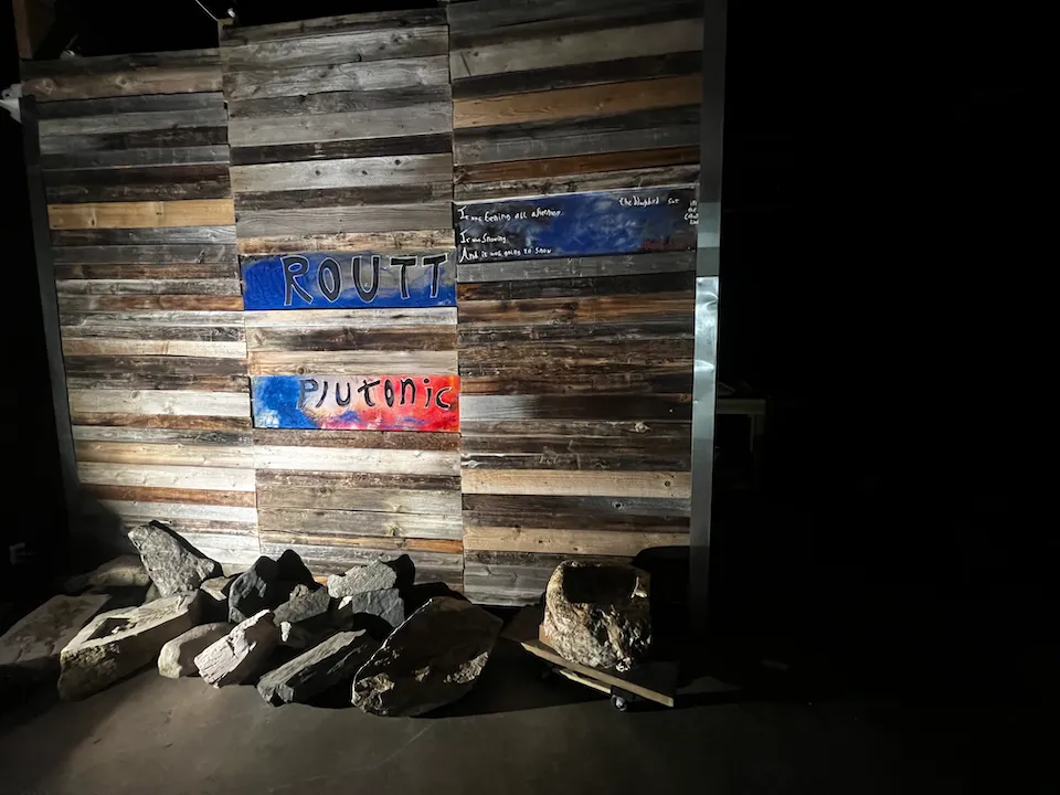 Painted Routt Plutonic sign on a reclaimed-wood wall at the shop, with raw stones piled below